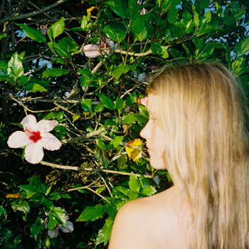Alice Phoebe Lou — profile view with blonde hair, facing a hibiscus flower