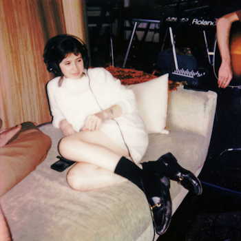 Clairo — sitting on a couch wearing headphones in a warm-toned film photo