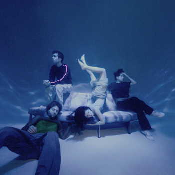The Marías — band members posed on a bed in blue-tinted light